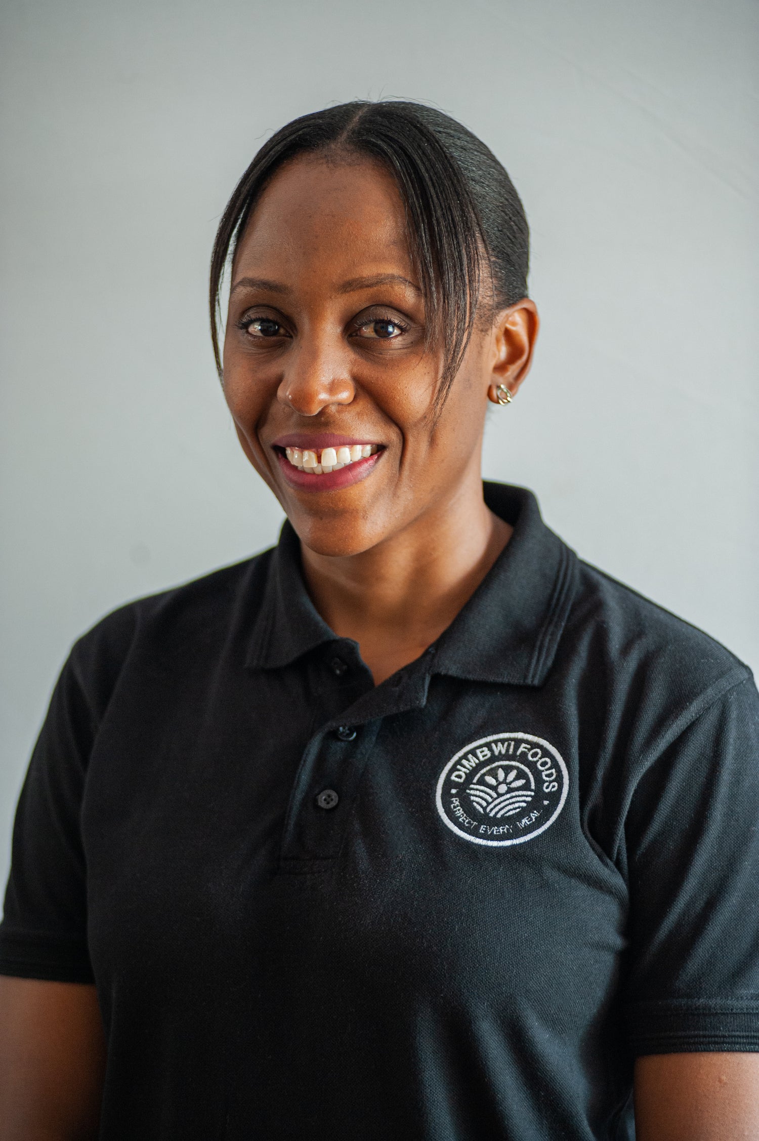 Portrait of Mwansa Kopa - Mkandawire Co-Founder of Dimbwi Foods in a black golf t-shirt with the Dimbwi Foods Logo in white